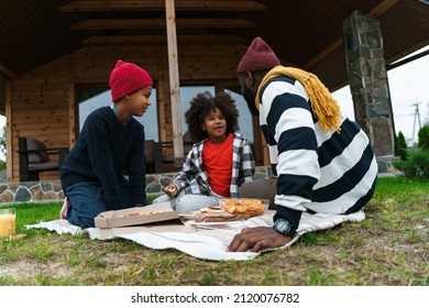 Black Father And His Sons Laughing And Eating Pizza While Resting Outside City