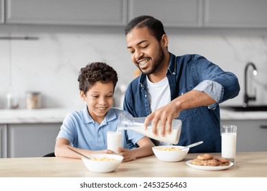 A black father pours milk into his son's glass, showcasing a moment of care and teaching in a family-oriented kitchen environment - Powered by Shutterstock