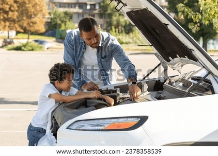 Black father and preteen son checking car engine outdoors. African american dad and school aged kid standing next to open automobile hood, fixing broken auto, traveling together