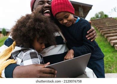 Black Father Smiling And Using Laptop While Resting With His Sons Outside City