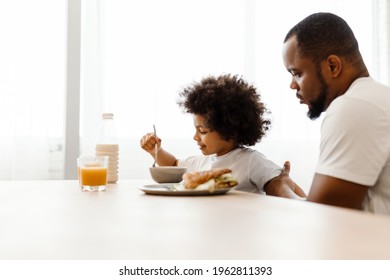 Black father and son having breakfast while sitting at table in home kitchen - Powered by Shutterstock