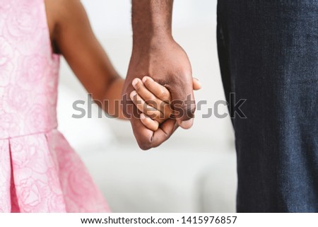 Black father taking his little daughter gently by the hand, giving her warm, safe, protected and comforting feeling, closeup