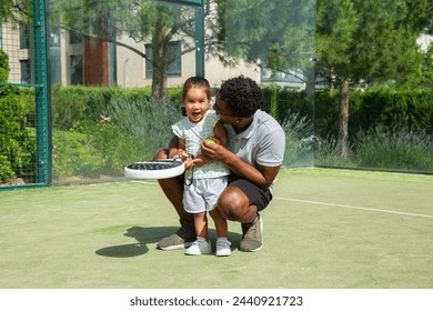 Black father teaching happy daughter to play paddle tennis	 - Powered by Shutterstock