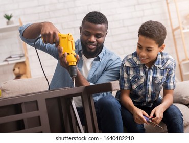 Black Father Teaching His Son How To Use Drill, Perforating Chair In Living Room At Home, Sharing Experience