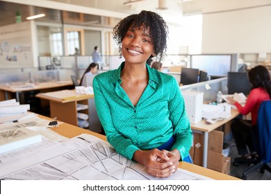 Black Female Architect Leans On Desk Smiling In Busy Office