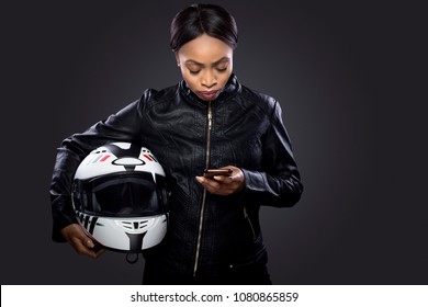Black female biker or motorcycle rider looking at mobile phone for GPS map.  She is looking up her location for navigation while traveling.  The image depicts technology app for transportation.