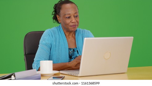 Black female business professional using laptop at her desk on green screen