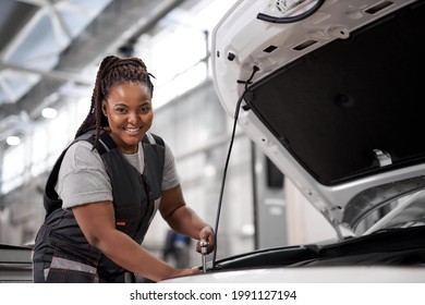 Black Female car mechanic holding wrench checking up on the car engine, for repair and checkup, wearing overall, repairing auto hood. side view portrait. copy space