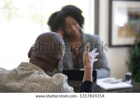 Black female client is upset at tax preparer or CPA accountant in an office.  The image can also depict a manager angry at a secretary.