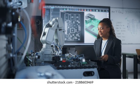 Black Female Developer Controls Robot Hand With Laptop, While Writing Code At Computer Science Research Laboratory. High-Tech Science And Programming At Modern Start Up Lab Concept.