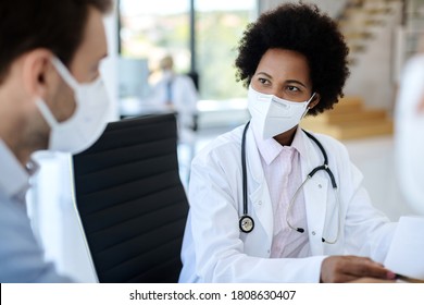 Black female doctor communicating with a patient while wearing protective face mask during medical appointment. 