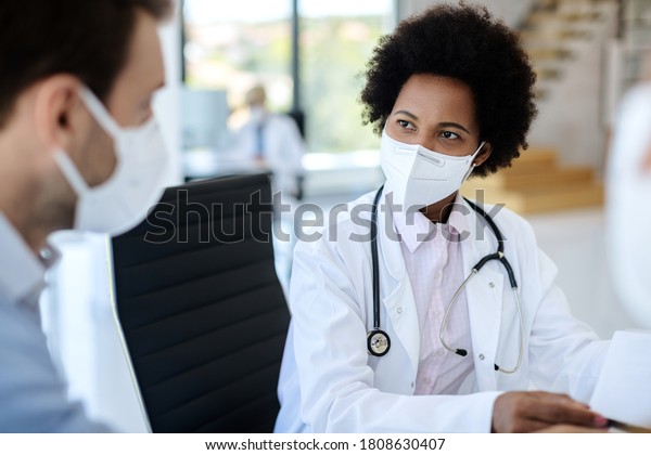 Black female\
doctor communicating with a patient while wearing protective face\
mask during medical appointment.\
