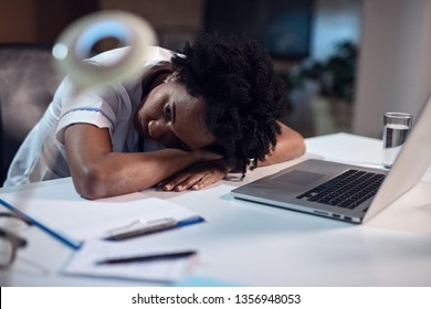 Black Female Doctor Feeling Exhausted And Relaxing While Leaning On Her Desk During Late Night Shift. 