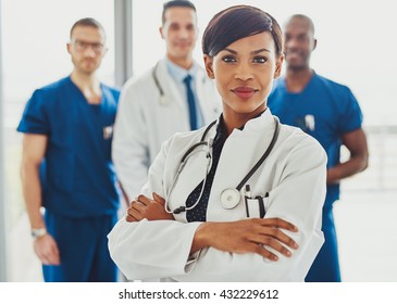 Black Female Doctor In Front Of Team, Looking At Camera With Medical Team In Background