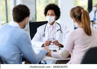 Black female doctor talking to a couple while wearing protective face mask during counseling at doctor's office. 