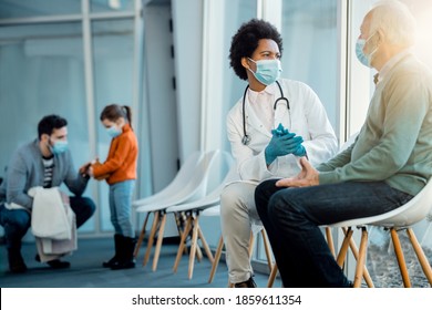 Black Female Doctor Talking To Senior Man In A Waiting Room At Medical Clinic During Coronavirus Pandemic. 