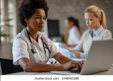 Black Female Doctor Using Computer While Typing Medical Reports In Her Office. 