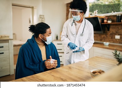 Black Female Doctor Using Digital Tablet While Visiting Sick Man At Home Due To Coronavirus Pandemic. 