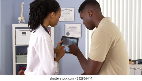 Black Female Doctor Using Tablet Computer To Share X Ray With Patient