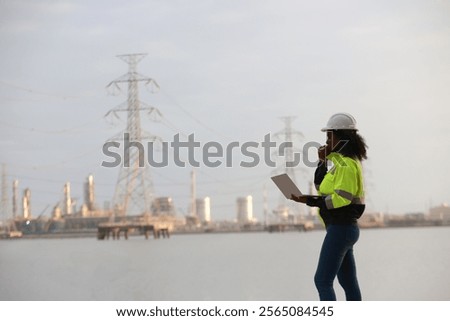 A Black female electrical engineer using a laptop computer to stand at the electricity station to see the electric power production plan at a high voltage electrode at the pier