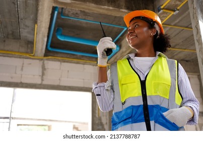 A Black Female Engineer Working At A Construction Site, She Wears A Hard Hat,a Safety Helmet, And A Reflective Vest. In Her Hand Was A Radio.
African Woman Working Happily ,Success On Building A House