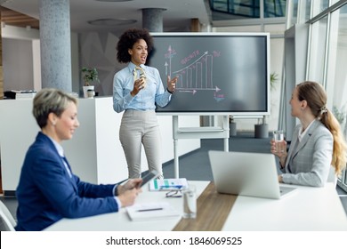 Black female entrepreneur giving a presentation about positive business growth to female colleagues in the office.  - Powered by Shutterstock