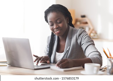 Black female entrepreneur working in office, typing on laptop computer and taking notes, free space