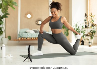 Black female fitness blogger stretching in front of smartphone at home, shooting video for her followers. Fit african american lady having personal training online - Powered by Shutterstock