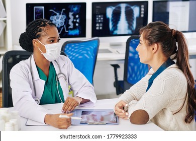 Black Female General Practitioner In Medical Mask Discussing X-ray With Serious Patient And Giving Her Recommendations