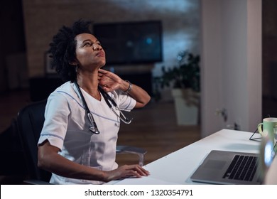 Black female healthcare worker experiencing neck pain during late night work at the office. 