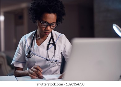 Black female healthcare worker reading medical records while working at doctor's office in the evening.  - Powered by Shutterstock