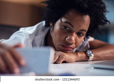 Black Female Healthcare Worker Using Mobile Phone And Taking Selfie While Feeling Bored During Late Night Shift. 