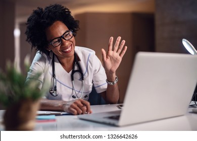 Black female healthcare worker waving and smiling while having video chat on the computer at doctor's office. 