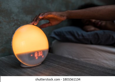 Black Female Lying In Bed And Turning Off Digital Alarm Clock After Awakening Early In Morning In Dark Room