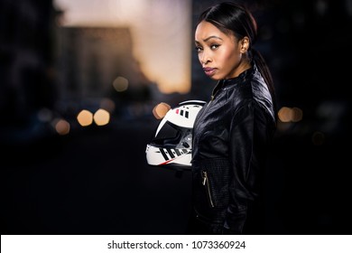 Black Female Motorcycle Rider Or Race Car Driver Wearing A Racing Helmet And Leather Jacket. Part Of The Gritty Woman Series, A Competitive Biker Or Racer Getting Ready For Competition.