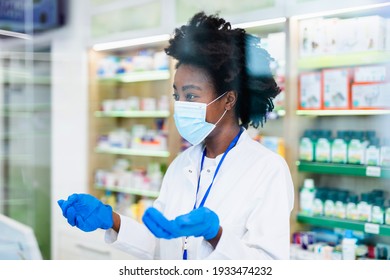 Black Female Pharmacist With Protective Mask On Her Face Working At Pharmacy. Medical Healthcare, Coronavirus, Covid-19 Concept.