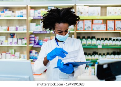 Black Female Pharmacist With Protective Mask On Her Face Working At Pharmacy. Medical Healthcare, Coronavirus, Covid-19 Concept.