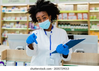 Black Female Pharmacist With Protective Mask On Her Face Working At Pharmacy. Medical Healthcare, Coronavirus, Covid-19 Concept.