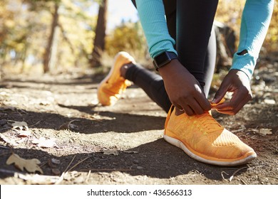 Black female runner in forest tying shoe, low section detail - Powered by Shutterstock