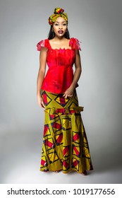 Black Female Showing African Pride By Wearing A Traditional Nigerian Dress And Head Scarf With Tribal Face Markings Or Cosmetic Makeup.  The Costume Is Red And Yellow And Shows Cultural Fashion.