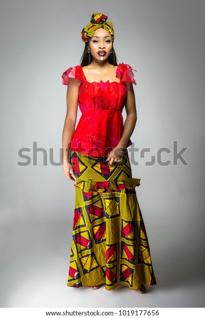 ナイジェリアの伝統的なドレスと頭のスカーフを着て 部族の顔の印や化粧の化粧をし アフリカの誇りを表す黒い女性 衣装は赤と黄で 文化的なファッションを見せる の写真素材 今すぐ編集