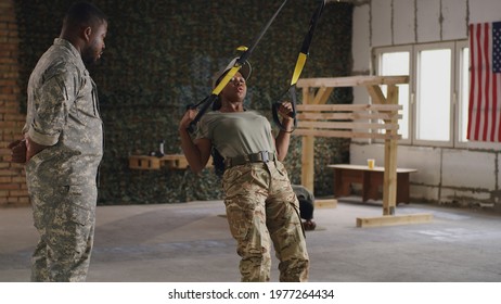 Black Female Soldier Exercising With TRX Ropes Near Trainer