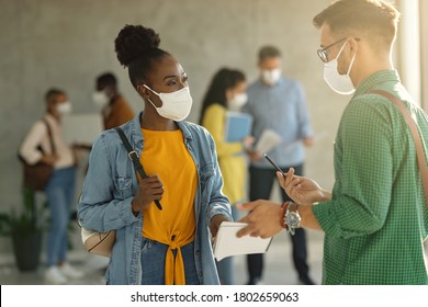 Black Female Student Ad Her Friends Wearing Protective Face Masks While Communicating At University Hallway. 