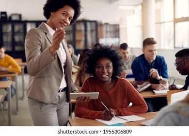 Black female student writing notes while teacher is explaining lecture on a class in the classroom. - Shutterstock ID 1955306809