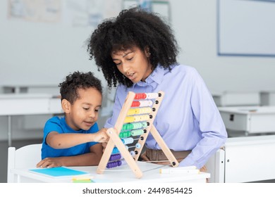 Black female teacher and little boy sitting at desk doing math using abacus, early education concept - Powered by Shutterstock