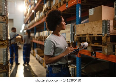 Black Female Warehouse Worker Going Through Delivery Schedule While Checking Stock In Storage Room.