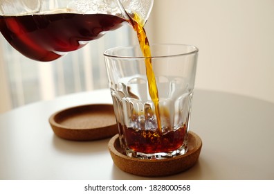 Black filter coffee pours from a jug into a glass close up. Specialty third wave concept. Light background