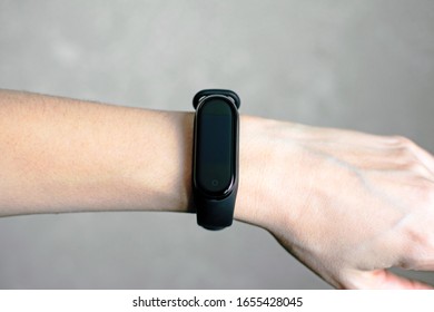Black fitness bracelet for sports training on a girl's hand on light coloured background. Selective focus.