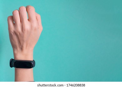 Black fitness bracelet for sports training on a girls hand on mint background. Selective focus.