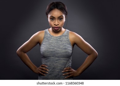 Black Fitness Trainer Or Athlete Posing As A Gritty Woman On A Dark Background.  She Is Fit And Slim.  The Image Depicts Female Sports And Health. 